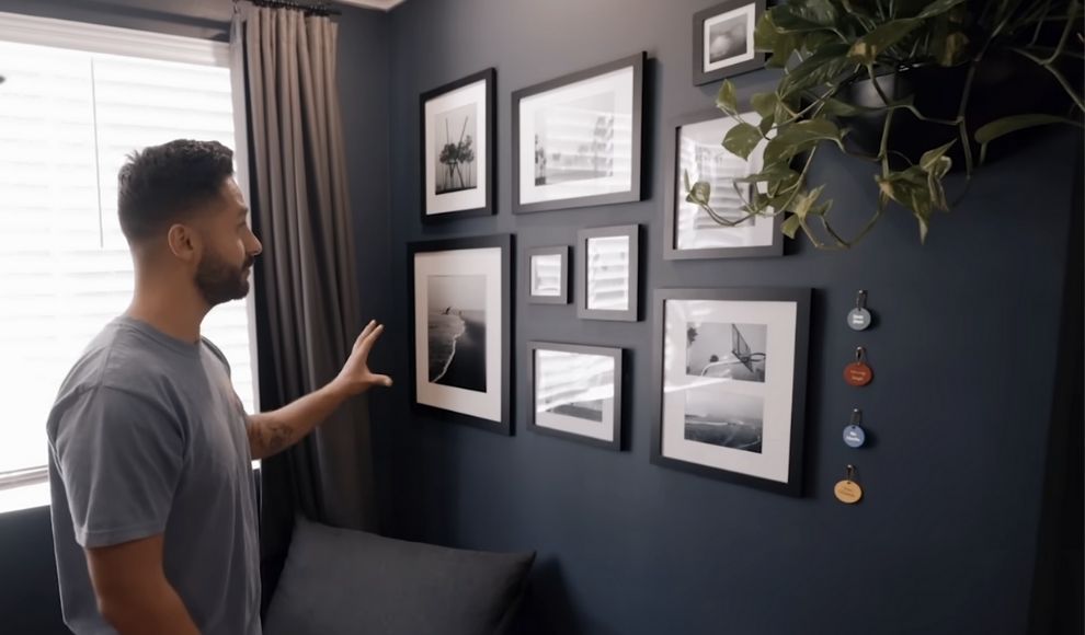 Covek posmatra zid sa rasporedjenim ramovima i dekorom, koji vizuelno odvaja jednu funkcionalnu celinu u sobi