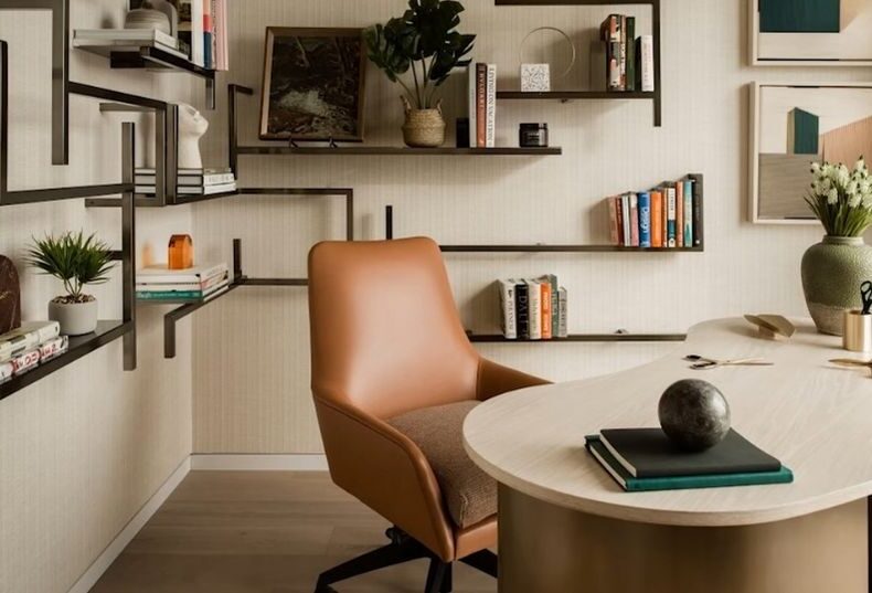 Svetao minimalisticki radni prostor sa zidnim policama, knjigama, biljkama i koznom stolicom pored okruglog stola