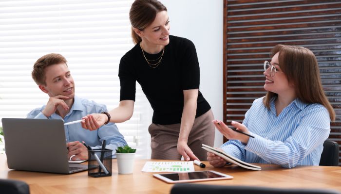 Tim zaposlenih sarađuje u kancelariji za stolom uz laptop i dokumenta tokom zajedničkog rada na projektu.